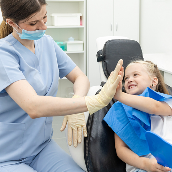 Child in dental chair high fiving dental team member