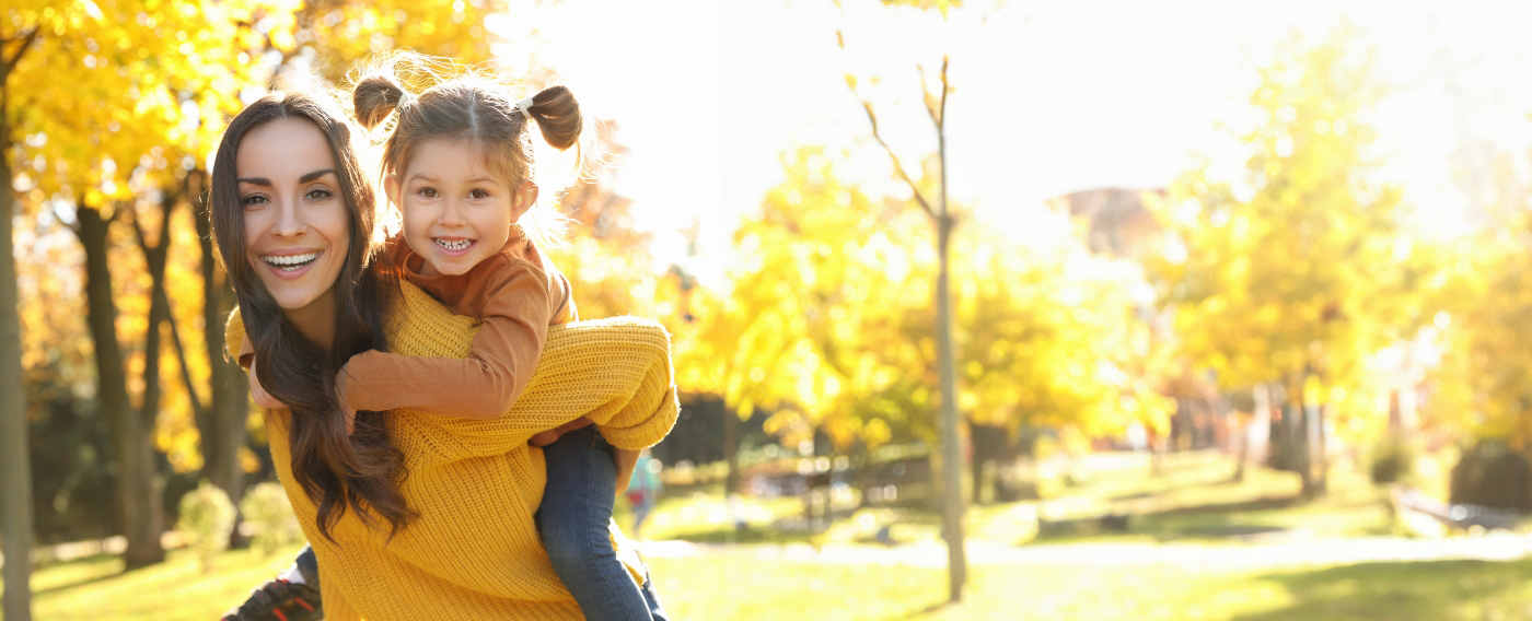 Smiling mother giving her daughter a piggyback ride outdoors