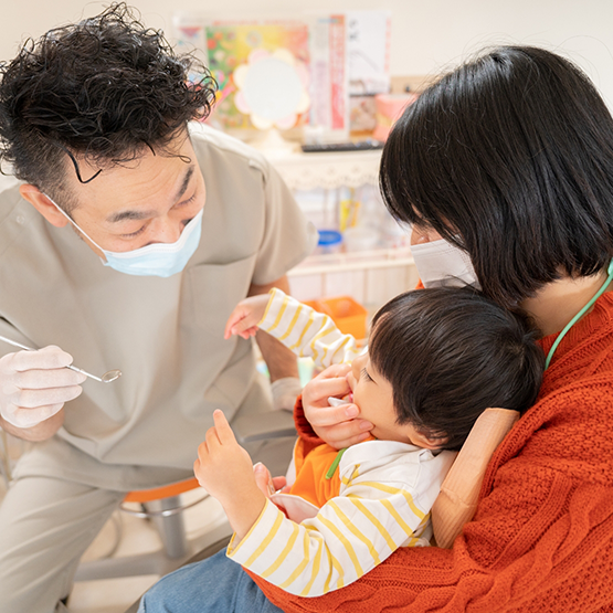 Pediatric dentist talking to a baby who is sitting in their mothers lap