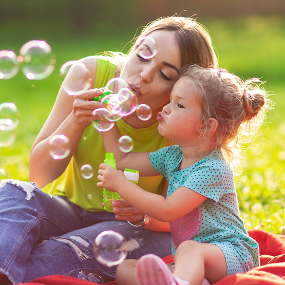 Mother and daughter blowing bubbles while sitting in grass