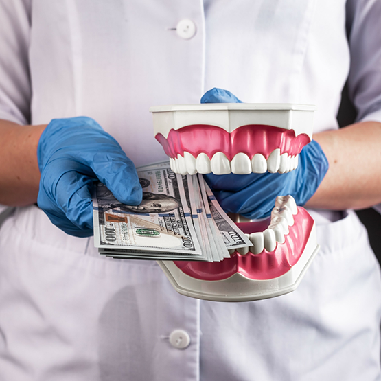 Dentist holding a model of the teeth in one hand and a stack of cash in the other