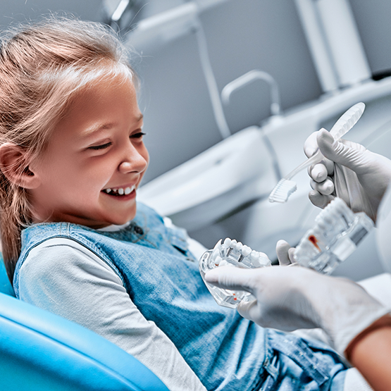 Dentist showing a young girl a model of the teeth and a toothbrush