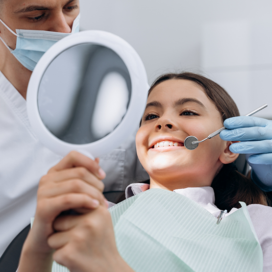 Young girl in dental chair looking at her smile in a mirror