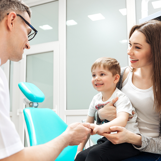 Pediatric dentist shaking hands with young boy in his mothers arms