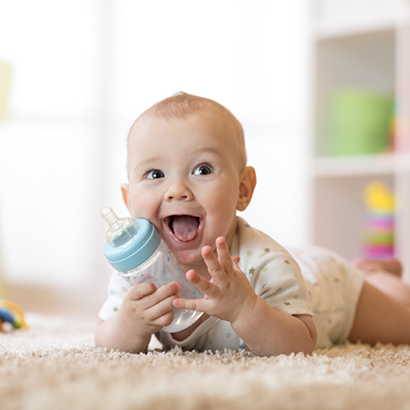 Baby laying on the floor and grinning while holding a bottle