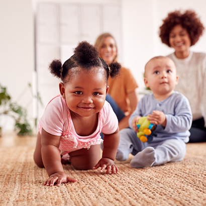 One baby sitting on floor next to a crawling baby