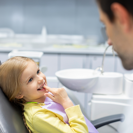 Young girl in dental chair pointing to her teeth