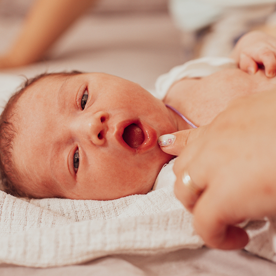 Baby laying down with adult pointing to their mouth