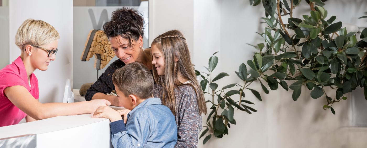 Dental team member showing a mother and two kids a paper at reception desk