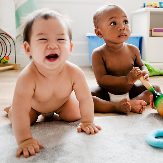 Two babies sitting on the floor with toys